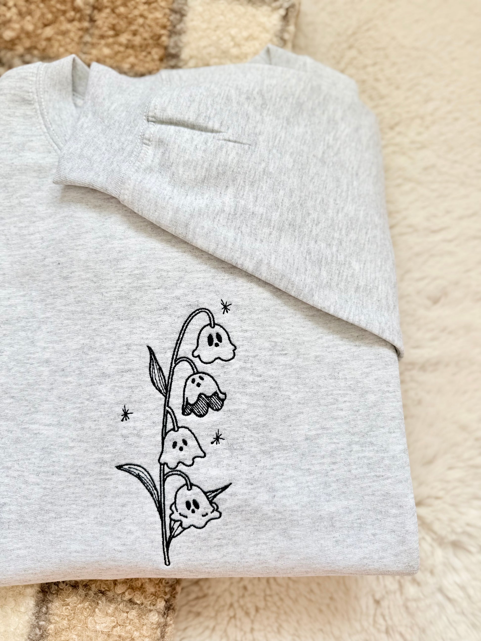 A whimsical twist on a classic botanical design, the "Ghost of the Valley" crewneck features delicate Lily of the Valley blooms transformed into subtle, charming little ghosts with embroidered sparkle accents. Minimalist, fine-line stitching gives this piece an understated cottagecore feel that works effortlessly for spooky season and beyond.

    Fine-Line Machine Embroidery: Crisp, detailed black linework designed to lay flat and hold up to daily wear.

    Subtle & Aesthetic: Perfect for those who prefer