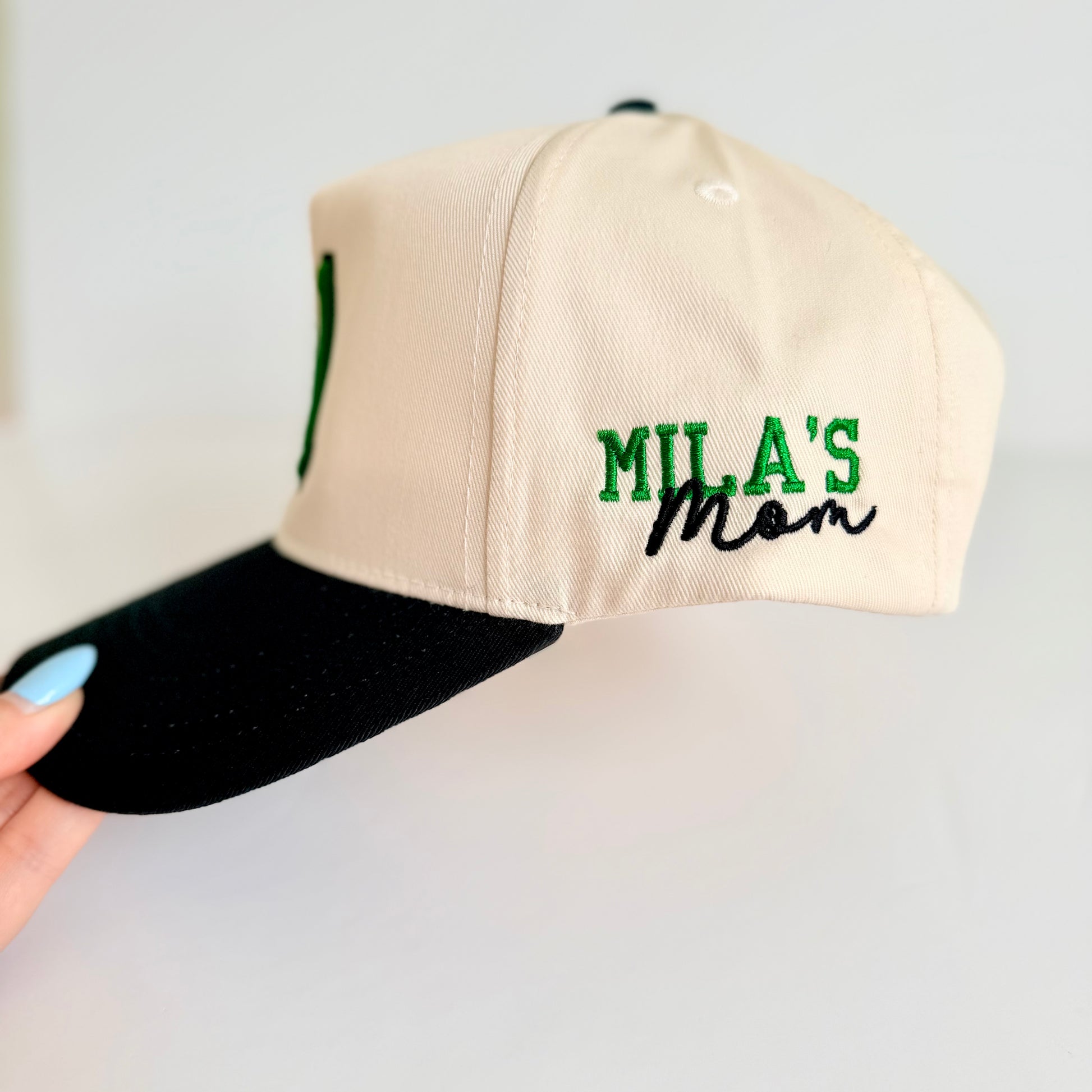 Beige cap with 'MILA'S Mom' text on a light gray background