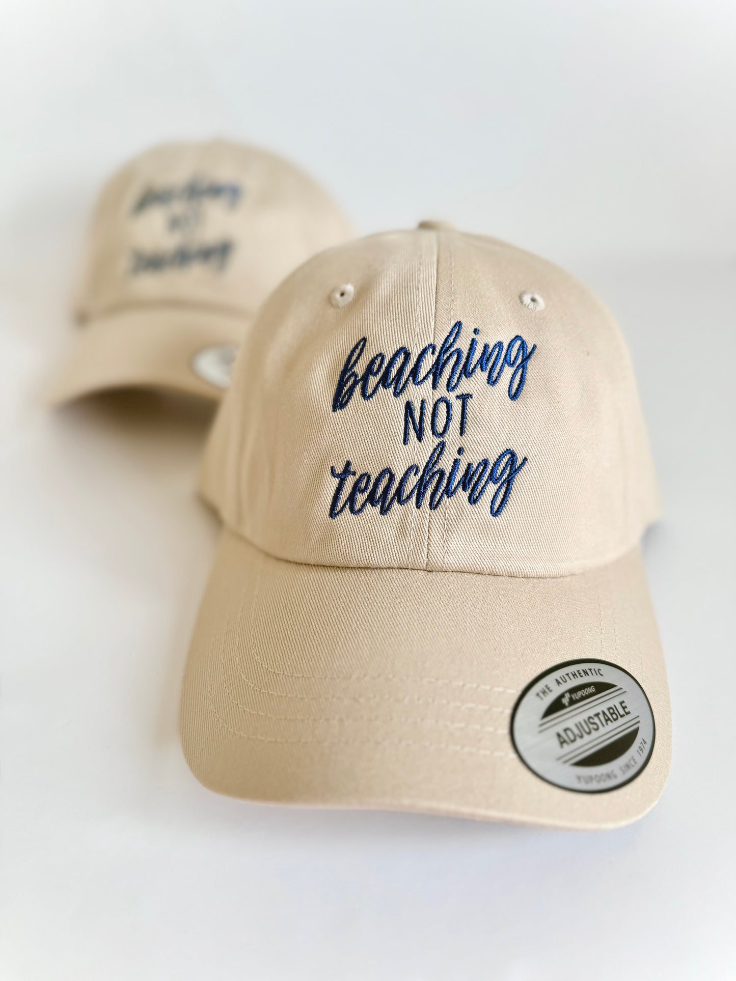 Beige cap with 'beaching not teaching' text on a white background. Embroidered custom hat stitched in Ontario, Canada. 