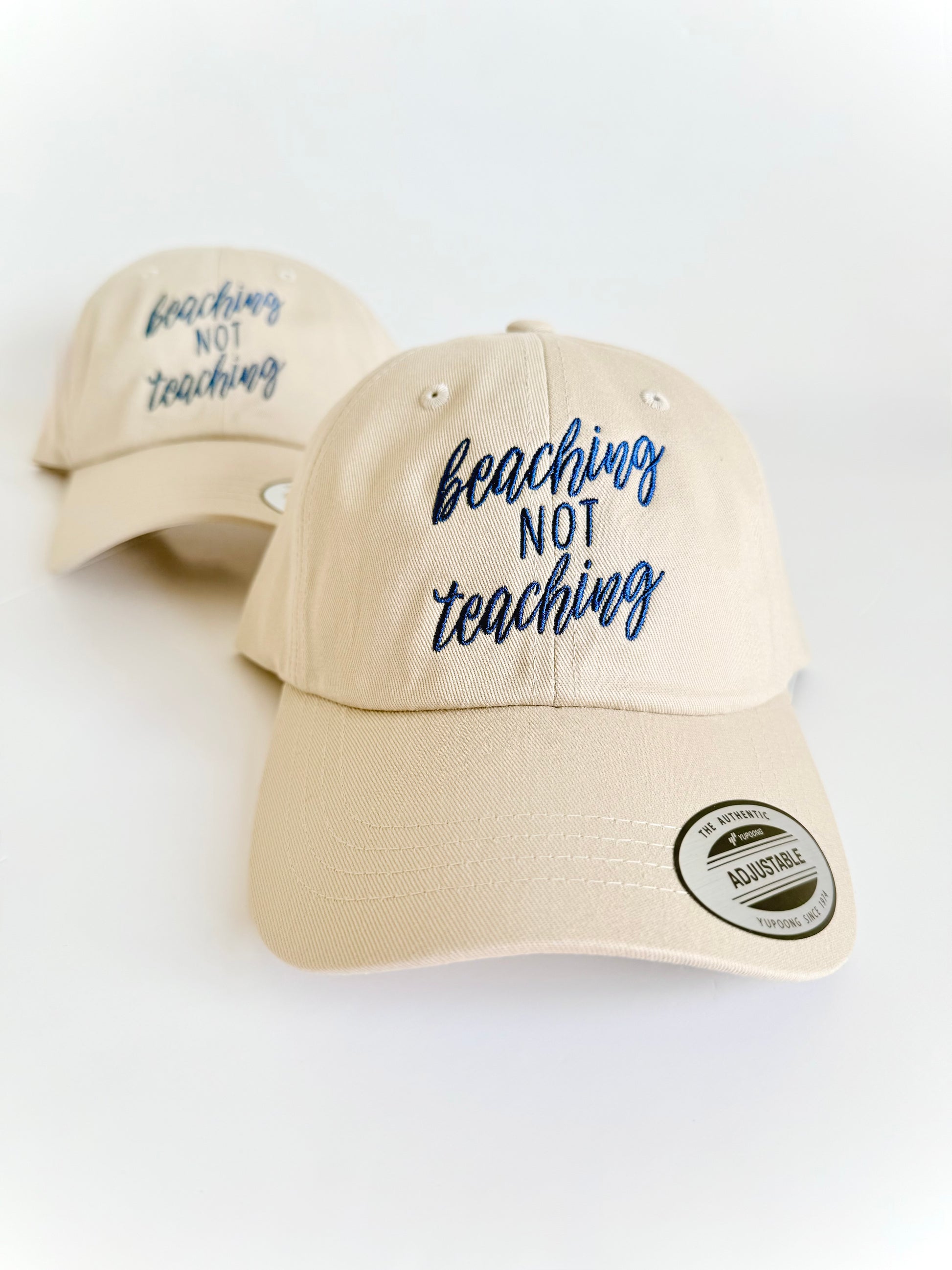 Beige cap with 'beaching not teaching' text on a white background. Embroidered custom hat stitched in Ontario, Canada. 