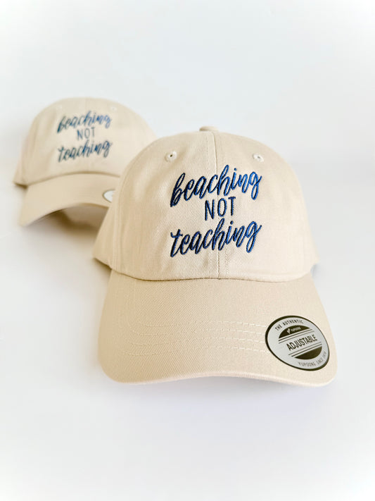 Beige cap with 'beaching not teaching' text on a white background. Embroidered custom hat stitched in Ontario, Canada. 