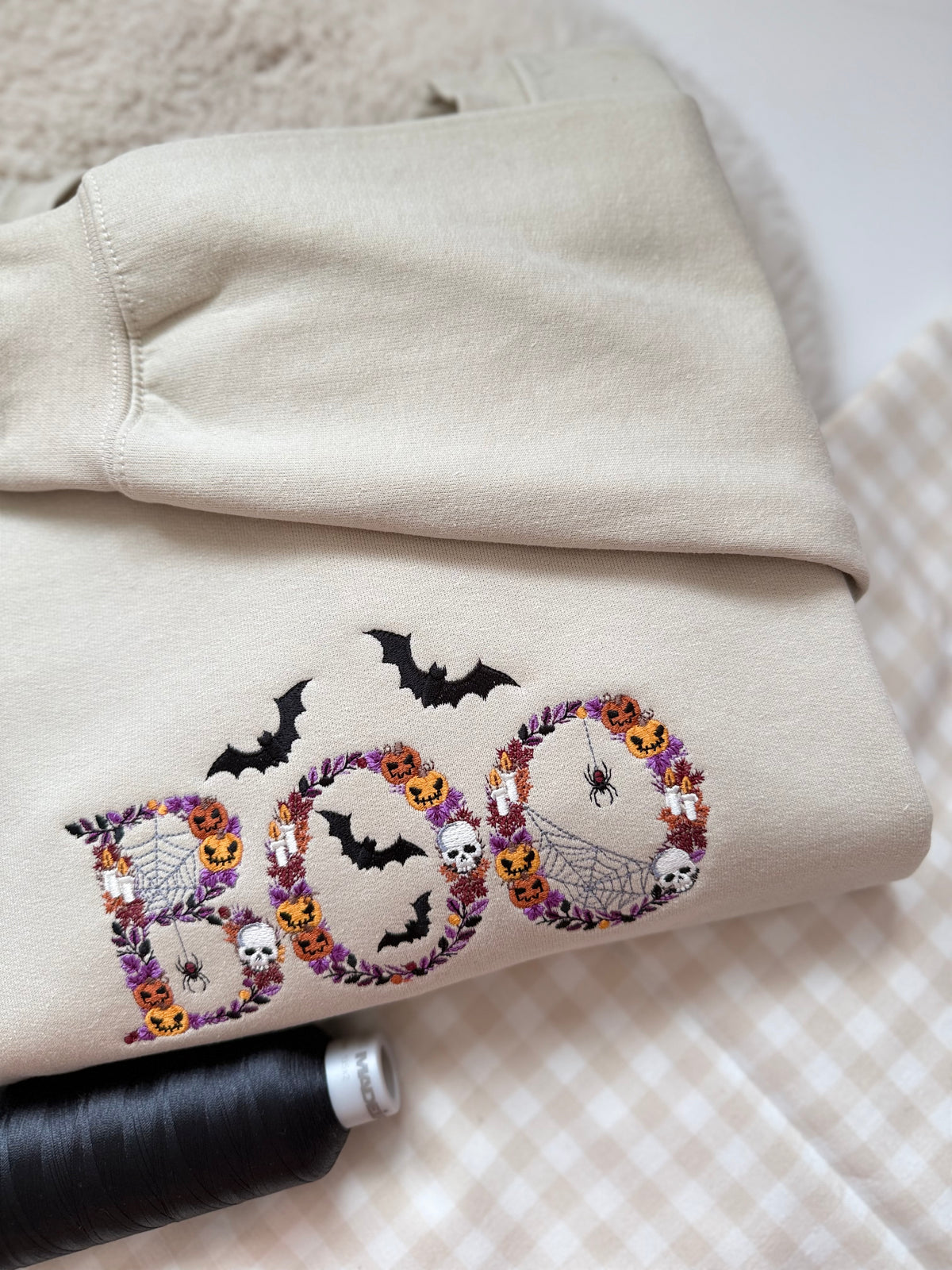 This piece features "BOO" crafted from rich purple floral vine wreaths woven with mini jack-o'-lanterns, skulls, candles, spider webs, and dangling spiders