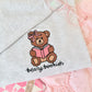 Gray sweatshirt with a teddy bear reading a book design and 'bearly bookish' text, surrounded by pink and white items.