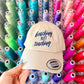 Beige cap with 'beaching not teaching' text on a white background. Embroidered custom hat stitched in Ontario, Canada. 