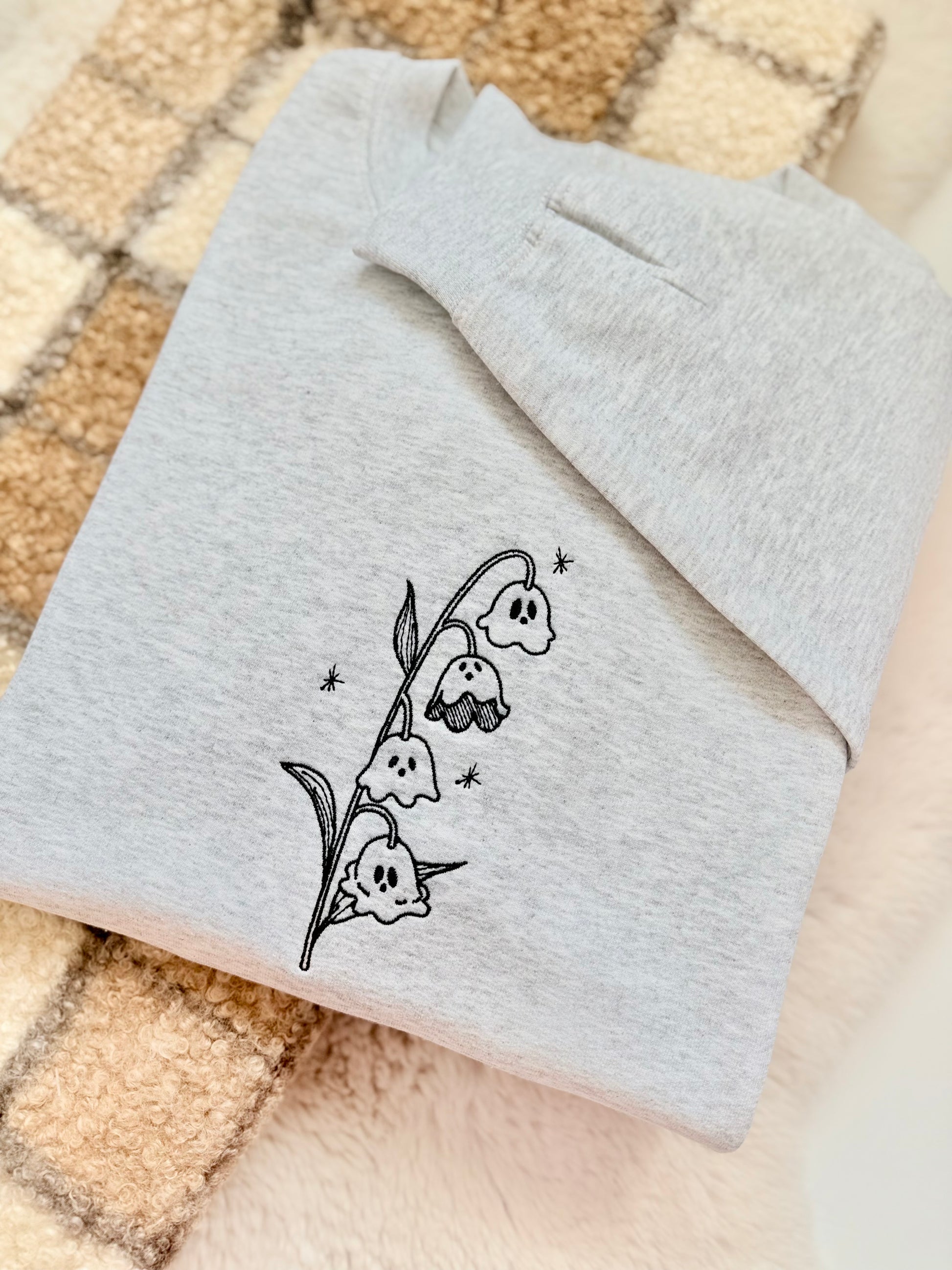 A whimsical twist on a classic botanical design, the "Ghost of the Valley" crewneck features delicate Lily of the Valley blooms transformed into subtle, charming little ghosts with embroidered sparkle accents. Minimalist, fine-line stitching gives this piece an understated cottagecore feel that works effortlessly for spooky season and beyond.

    Fine-Line Machine Embroidery: Crisp, detailed black linework designed to lay flat and hold up to daily wear.

    Subtle & Aesthetic: Perfect for those who prefer