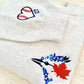 Embroidered fabric with a blue bird, red maple leaf, and white heart design on a beige background