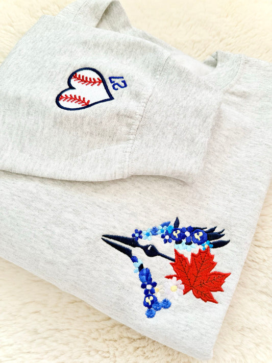 Embroidered fabric with a blue bird, red maple leaf, and white heart design on a beige background