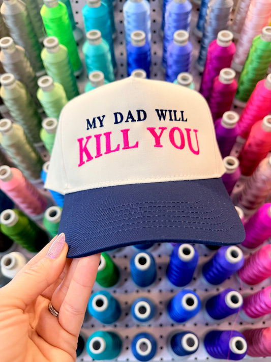 Cap with 'My Dad Will Kill You' text held in front of spools of colorful thread.