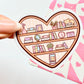 Heart-shaped sticker with a bookshelf design held by a hand on a pink heart-patterned background.