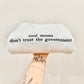 Sweater with 'cool moms don't trust the government' text embroidered held by a person with tattoos on a light background