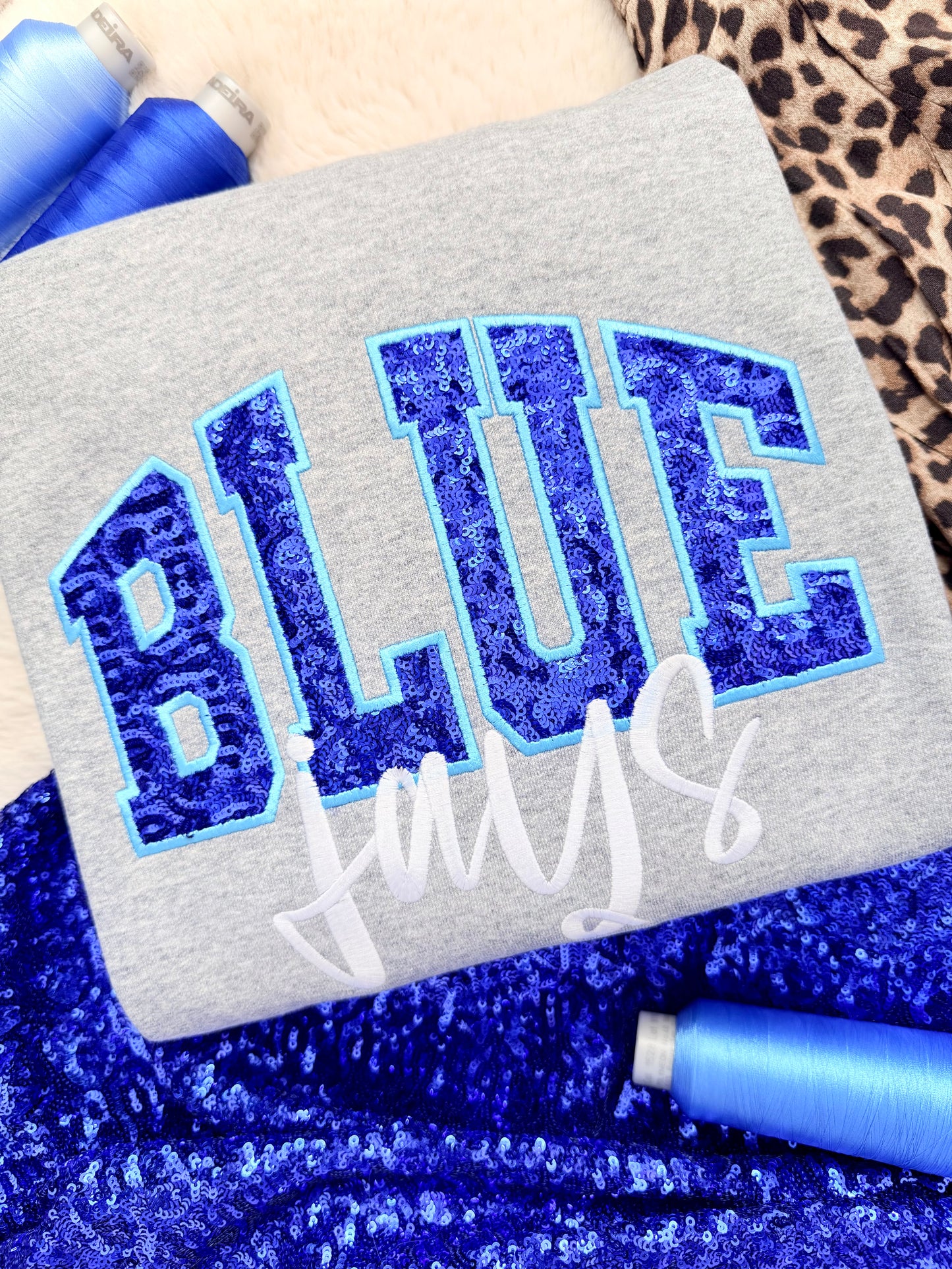 Gray fabric with blue glittery 'BLUE' text and white 'JAYS' text, surrounded by blue sequin applique embroidery.