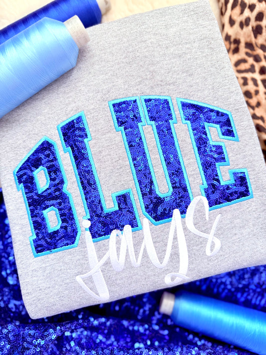Textile with 'BLUE Jays' embroidered in blue thread on a gray fabric background.