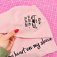 Pink sweatshirt with text and a hand holding it on a pink grid background