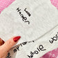 Gray fabric with embroidered text held by a hand on a pink cutting mat.