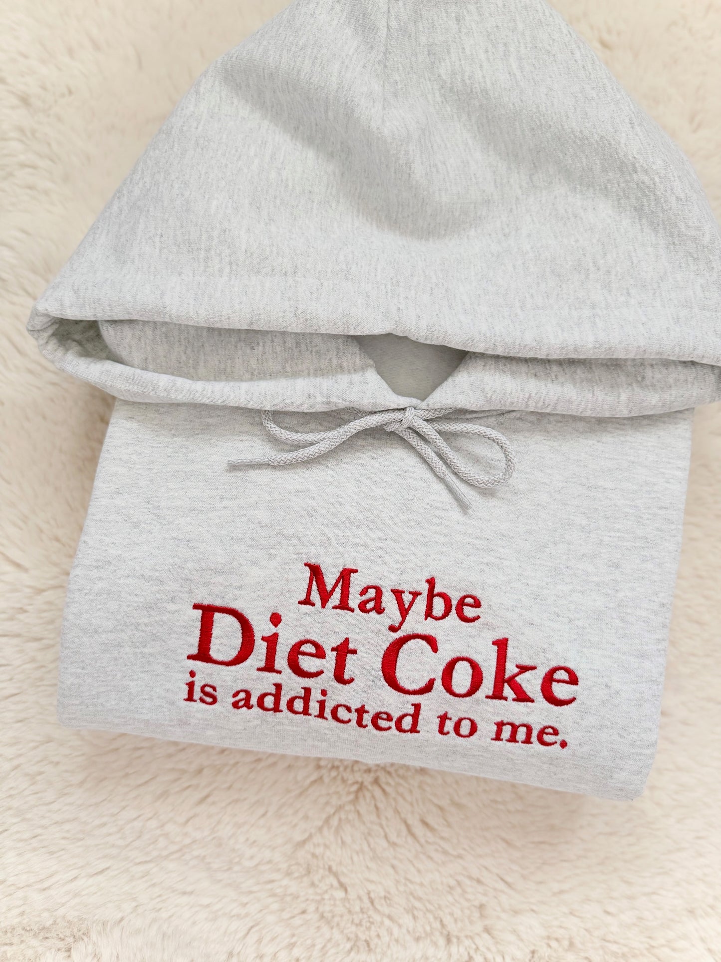 Gray hoodie with red text 'Maybe Diet Coke is addicted to me.' on a beige background