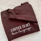 Folded brown sweatshirt with 'Coffee is my love language' text on a textured white surface