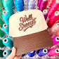 Cap with 'Well Sheeyit' text held in front of spools of colorful thread.