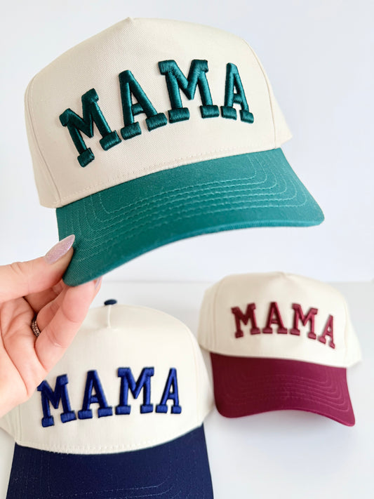 Three caps with 'MAMA' text in different colors held by a hand on a white background