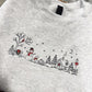 Bring a little holiday magic to your wardrobe with this cozy embroidered Christmas sweater. Featuring a charming winter village scene with a snowman, pup, sled, snowy trees, and a sweet little cottage, this design is perfect for the Christmas season.