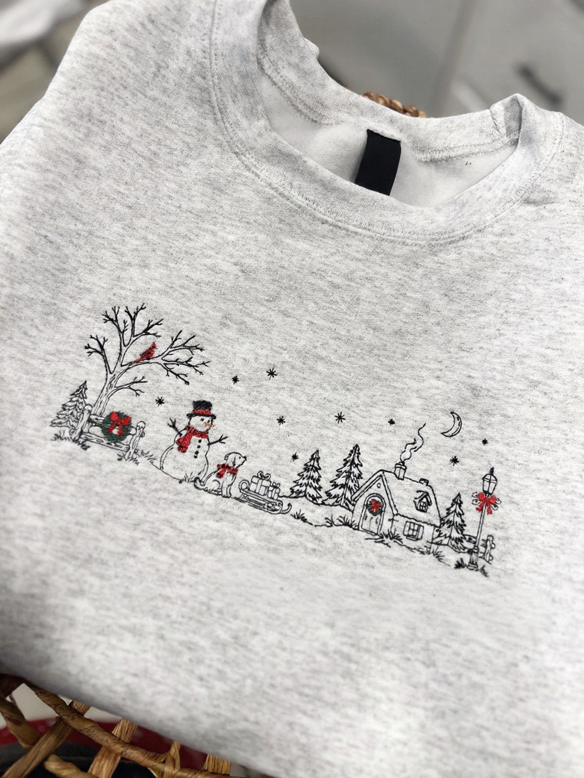 Bring a little holiday magic to your wardrobe with this cozy embroidered Christmas sweater. Featuring a charming winter village scene with a snowman, pup, sled, snowy trees, and a sweet little cottage, this design is perfect for the Christmas season.