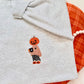 Gourd girl embroidered fall autumn sweater. Pumpkin head girl holding a coffee wearing a cozy sweater wearing pajama pants stitched onto a light grey sweater.