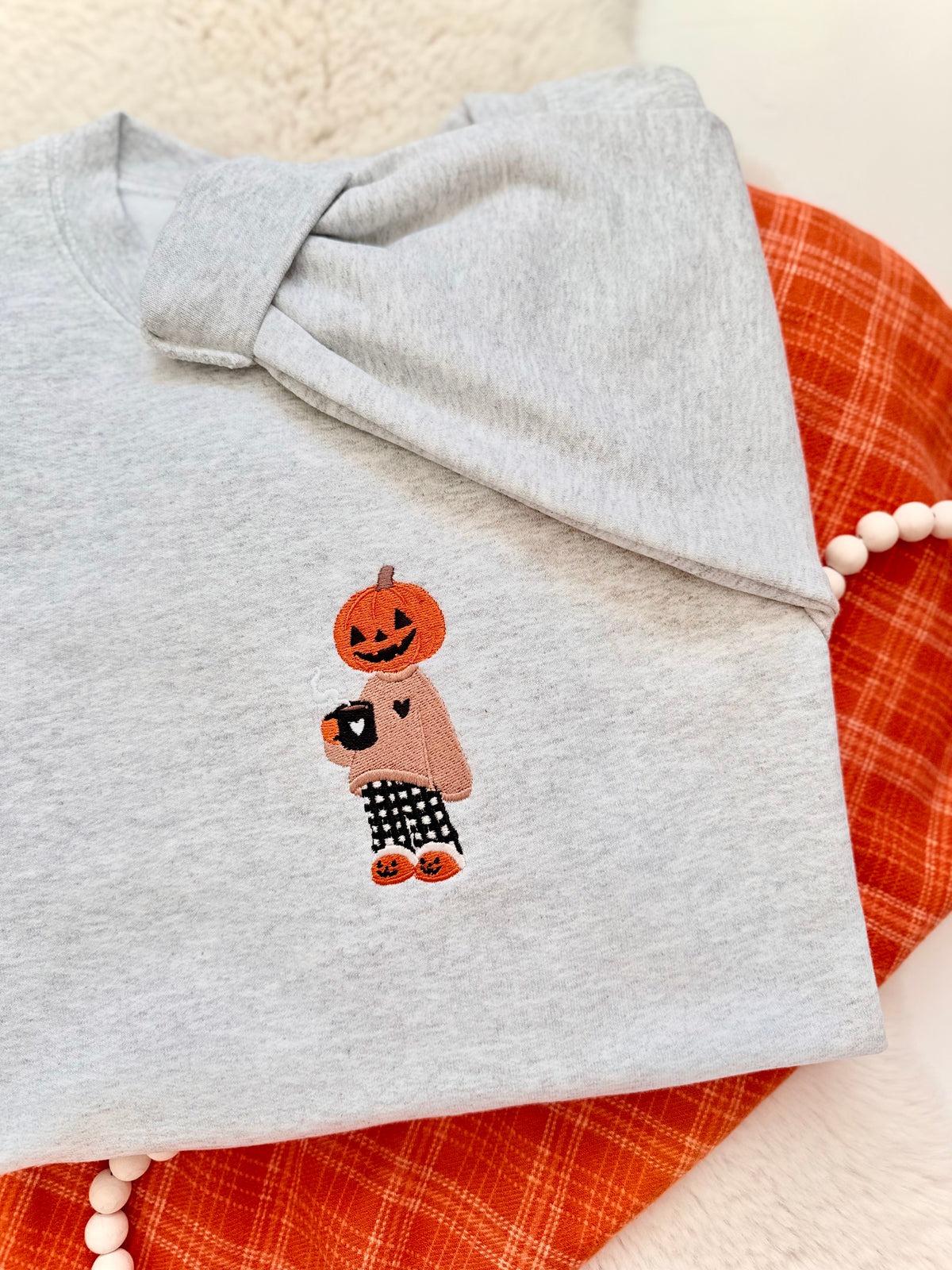 Gourd girl embroidered fall autumn sweater. Pumpkin head girl holding a coffee wearing a cozy sweater wearing pajama pants stitched onto a light grey sweater.