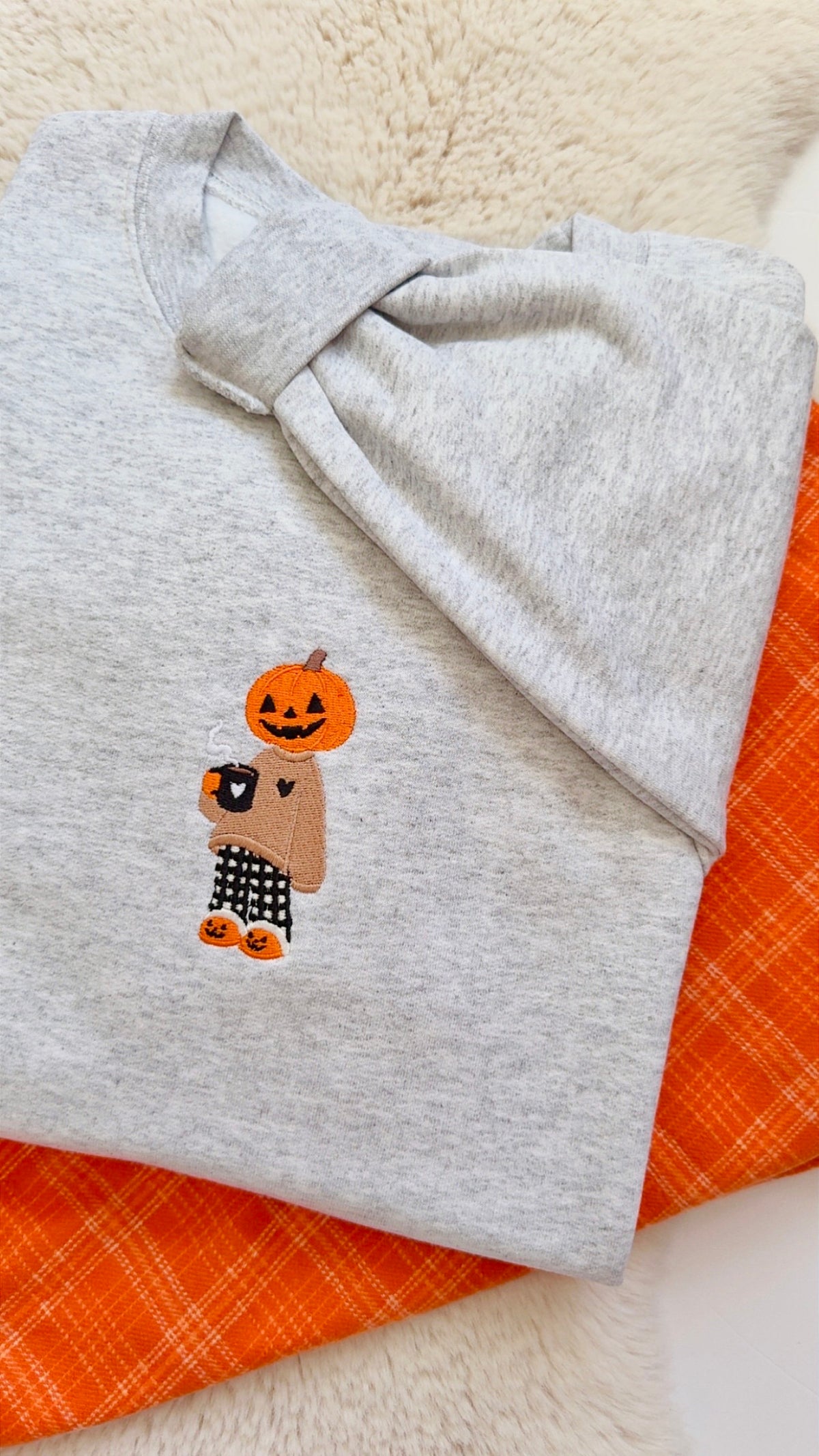 Gourd girl embroidered fall autumn sweater. Pumpkin head girl holding a coffee wearing a cozy sweater wearing pajama pants stitched onto a light grey sweater.